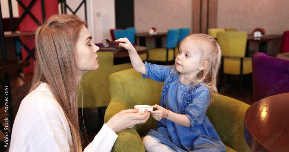 A funny little girl powders the nose of her young mother in a cafe. Happy family. A funny little girl powders the nose of her young mother in a cafe. Happy family.