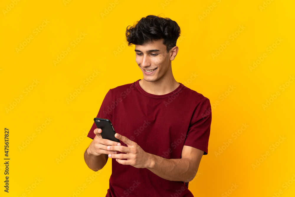 Young Argentinian man isolated on yellow background sending a message or email with the mobile Young Argentinian man isolated on yellow background sending a message or email with the mobile