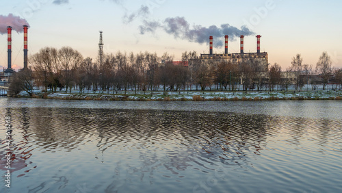 Smoking chimneys of thermal power plants near the waterfront in city. Winter. Industrial and nature background.