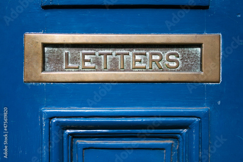 A metal mail slot on a door that says letters.  Mailbox for correspondence.  Wooden door with a metal letter / post slot.