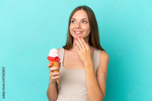 Young Lithuanian woman with cornet ice cream isolated on blue background looking up while smiling