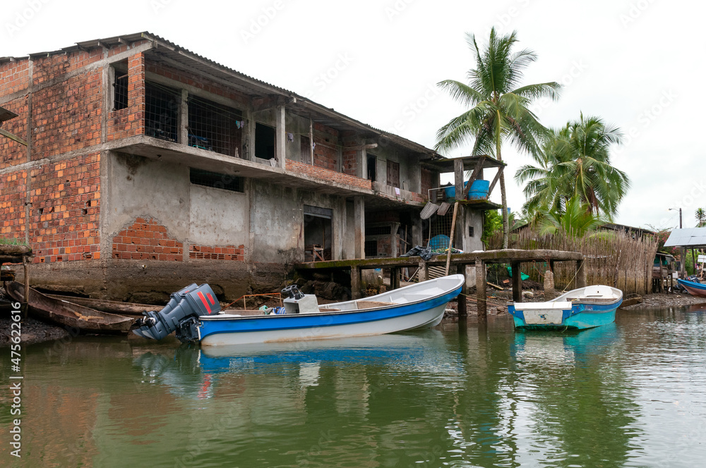 Outboard motor boat in front of a red brick house in a fishing village on the Colombian Pacific coast.