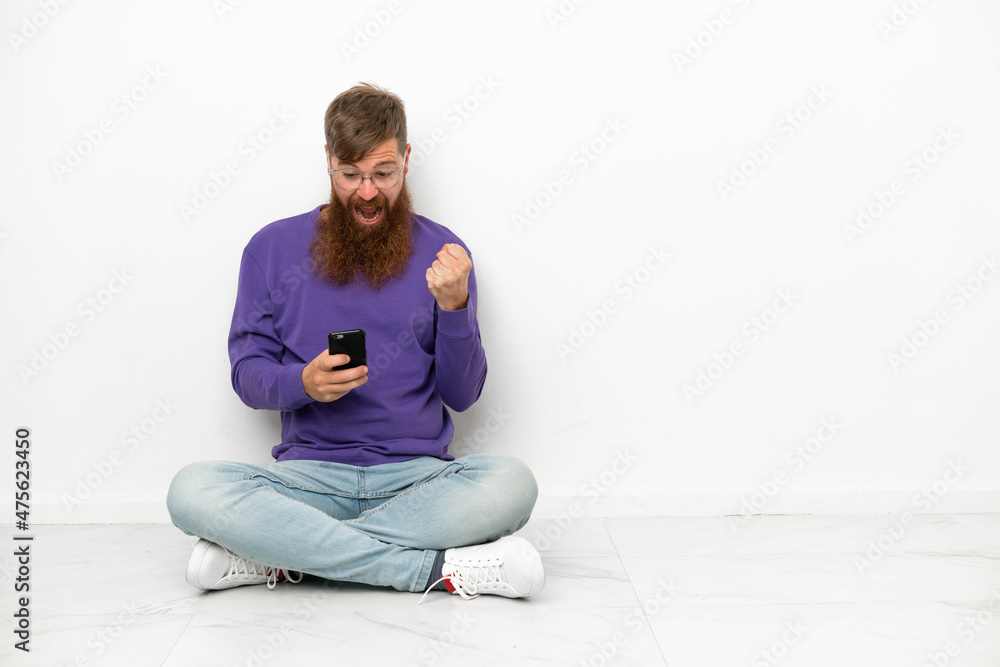Young caucasian reddish man sitting on the floor isolated on white background surprised and sending a message