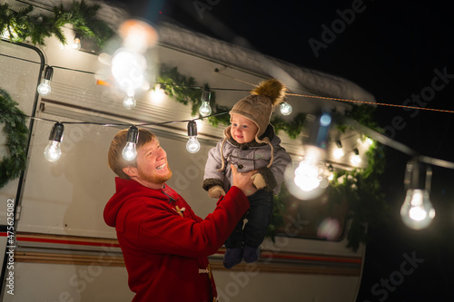 Caucasian red-haired man with a boy in his arms at the mobile home. Father and son celebrate Christmas on a trip.