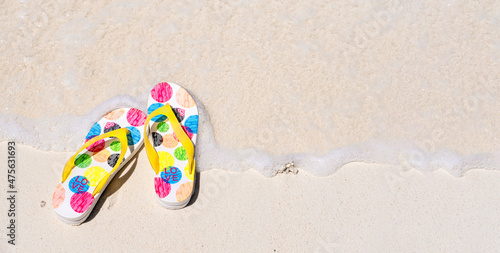 Summer flop flops or sandals on sandy beach by sea water, top view, copy space
