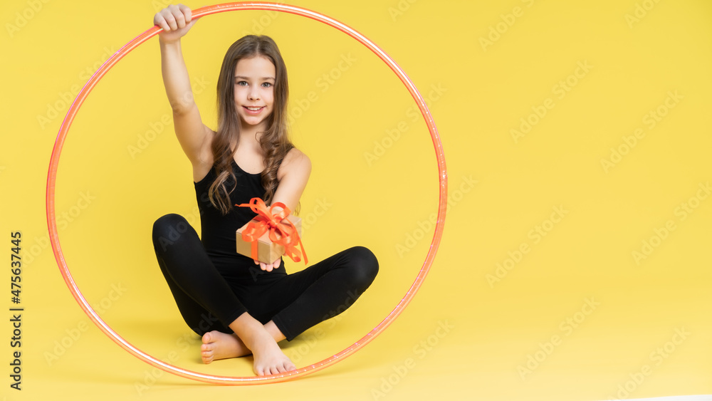 girl gymnast studio. little gymnast is sitting on the floor and looking at the camera. playing sports. Isolated on a colored yellow background.