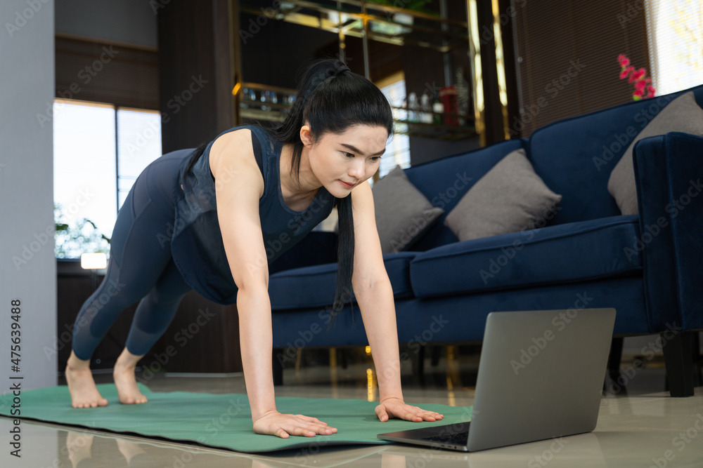 A young beautiful Asian woman learning physical exercise and workout online training program on a computer laptop at home A young beautiful Asian woman learning physical exercise and workout online training program on a computer laptop at home