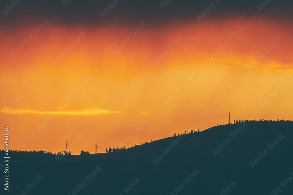Atmospheric landscape with dark silhouette of mountain with trees on background of vivid orange dawn sky. Colorful nature scenery with sunset or sunrise of illuminating color. Vivid sundown paysage. Atmospheric landscape with dark silhouette of mountain with trees on background of vivid orange dawn sky. Colorful nature scenery with sunset or sunrise of illuminating color. Vivid sundown paysage.