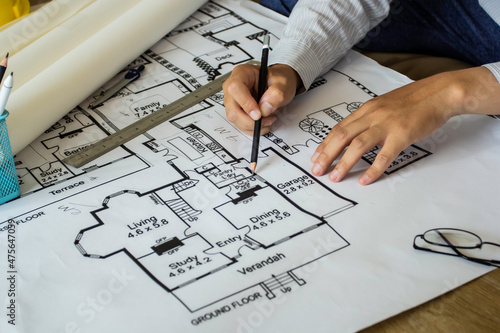 Young engineer holding a black pencil pointing to a building on blueprints for a workplace meeting, hands of an engineer working with tools on a background on a project sketch.