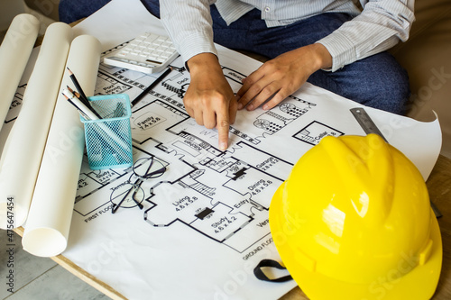 Young engineer pointing finger at a building on blueprints for a workplace meeting, engineer's hand working with tools on a background on a project draft.