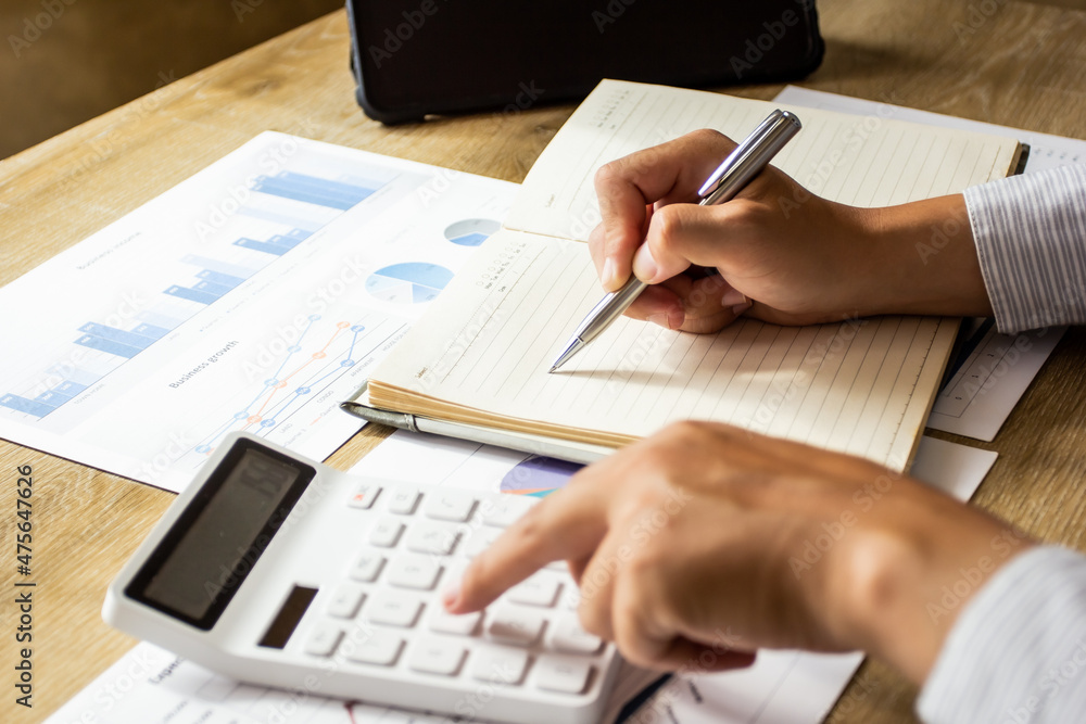 Young businessman calculates company income data and writes it down in a notebook to bring to meetings, businessman pointing to past company figures, business idea planning. Young businessman calculates company income data and writes it down in a notebook to bring to meetings, businessman pointing to past company figures, business idea planning.