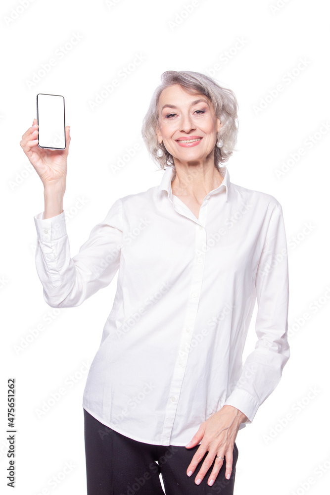 An attractive happy modern mature woman looks at the camera with a smile showing a smartphone in her raised hand isolated on white background An attractive happy modern mature woman looks at the camera with a smile showing a smartphone in her raised hand isolated on white background