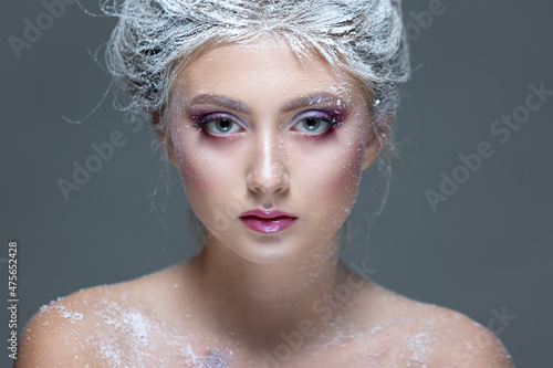 Winter Beauty Woman in clothes made of frozen flowers covered with frost, with snow on her face and shoulders. Christmas Girl Makeup. Make-up the snow Queen. Isolated on a gray background. Close-up. © satyrenko