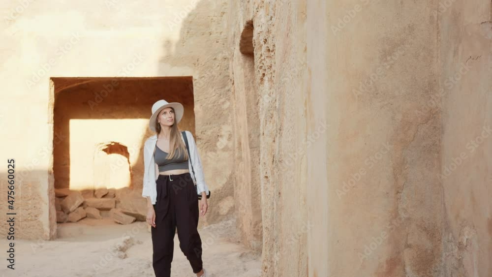 Competent female archeologist in white summer hat walking among ancient building with digital camera on neck. Concept of people, science and history. Focused woman examining ruins of ancient temple. Competent female archeologist in white summer hat walking among ancient building with digital camera on neck. Concept of people, science and history. Focused woman examining ruins of ancient temple.