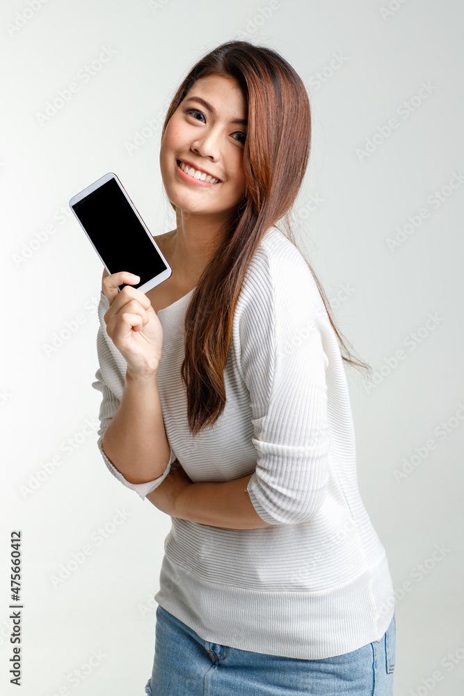 Portrait studio shot Asian young pretty female model in long sleeve shirt show naked shoulder and short denim skirt stand hold black blank screen smartphone for ads look at camera on white background Portrait studio shot Asian young pretty female model in long sleeve shirt show naked shoulder and short denim skirt stand hold black blank screen smartphone for ads look at camera on white background