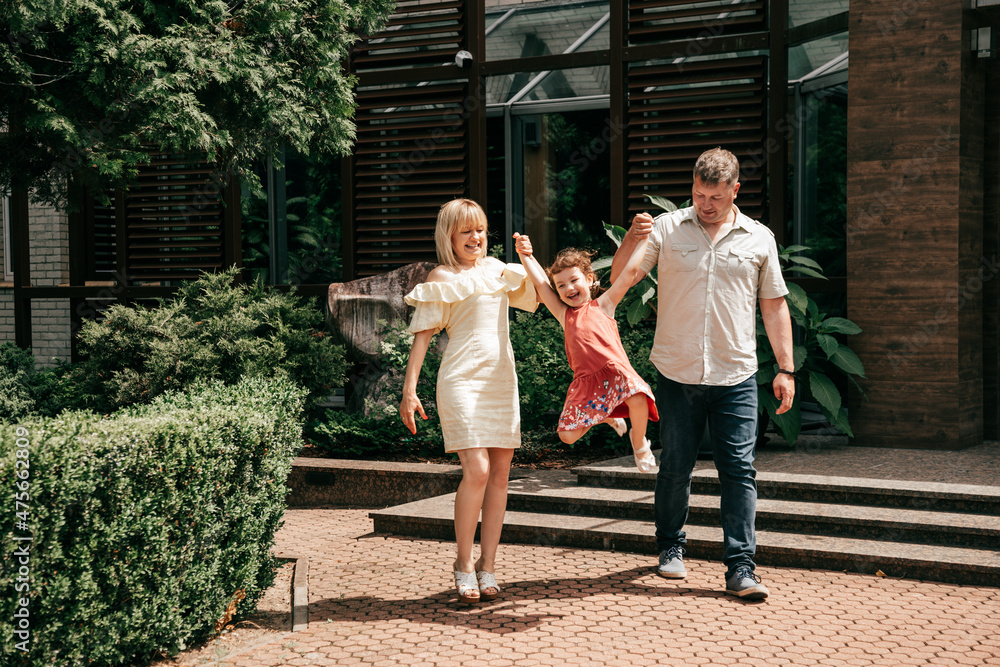 Fototapeta premium Family with little girl having fun at hotel on vacation. Full family. Happy relationship. Right way of life. Role model. Rest at hotel. Travel and tourism. City park.