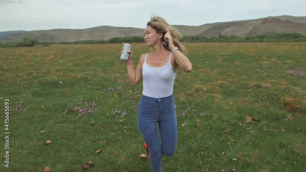 Camera follow hipster young woman in white t-shirt short jeans fluttering long hair. One girl dancing to the portable music speaker on smartphone. Camera follow hipster young woman in white t-shirt short jeans fluttering long hair. One girl dancing to the portable music speaker on smartphone.