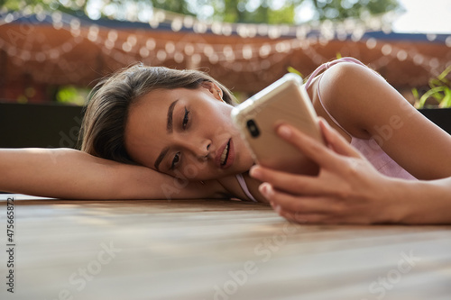 young asian pretty woman with long hair lays her head on her arms and table, holding phone in hand. beautiful sensual lady laying at cafe, using smartphone. lifestyle portrait