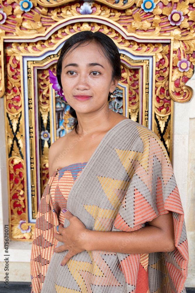 Portrait young woman with balinese face, wearing dress traditional Bali sarong in home door.