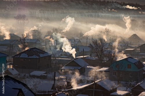 Village in Siberia during the morning. The view from the top. Many wooden houses in the countryside with stove heating. Frosty day.