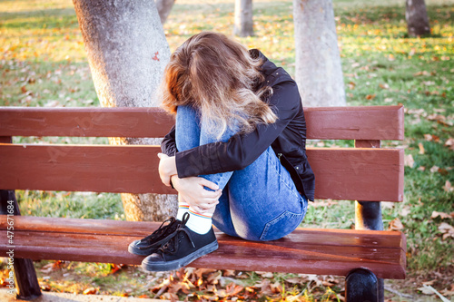 Sad teenager girl sitting on the bench in autumn park. Crying young girl in depression