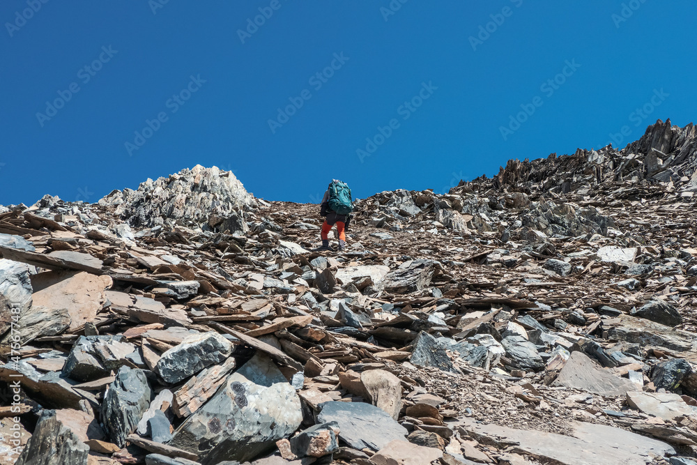 Heavy climbing on a steep stone slope. Solo trekking in the mountains. Travel photographer lifestyle, hiking hard track, adventure concept in spring vacation.