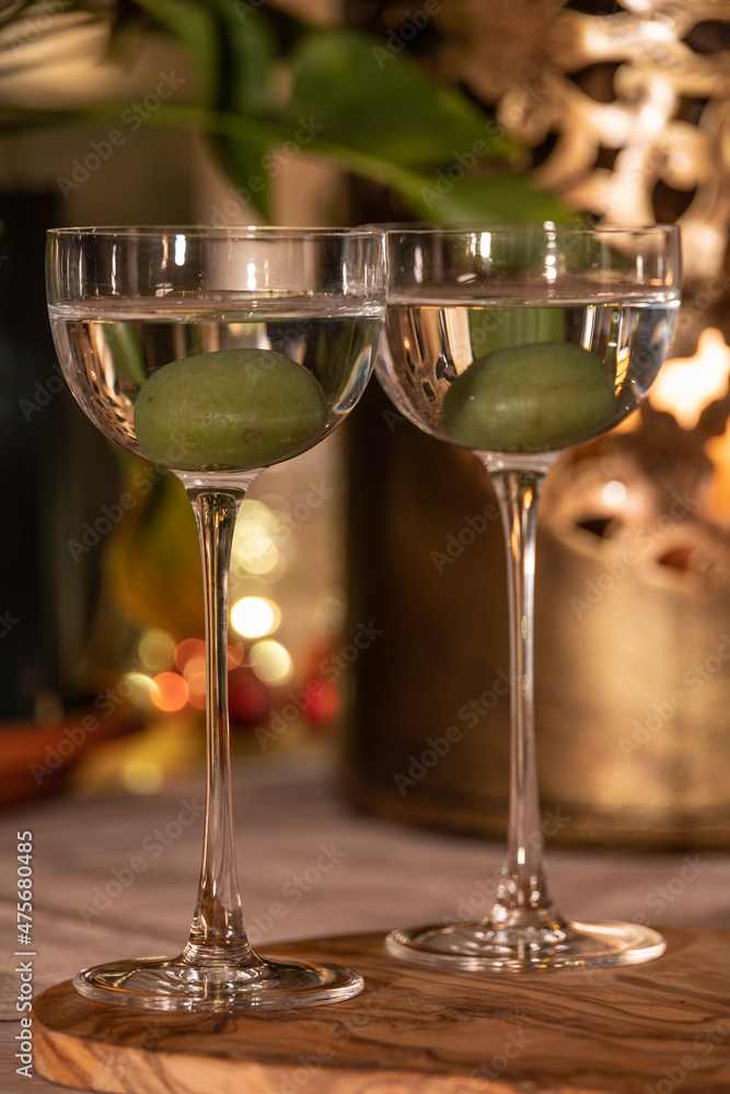 Close up shot of two martini cocktails with olive in beautiful, vintage pony glass. Bokeh lights in background. Indoor, cozy, warm festive atmosphere, crisp and high clarity edit.