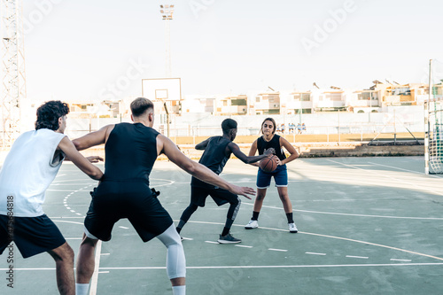 Woman and three men playing basketball in an urban court
