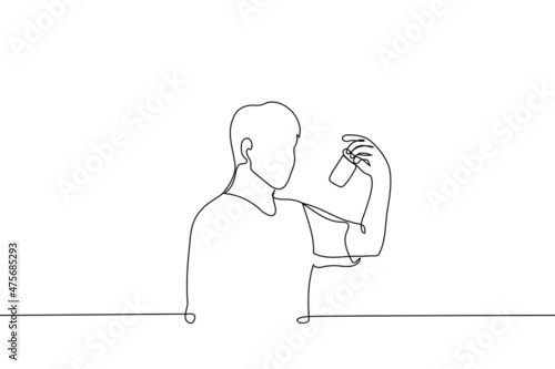man stands looking at a jar of tablets or pills - one line drawing vector. concept of buying medicines, reading the composition of ingredients from medicines and supplements