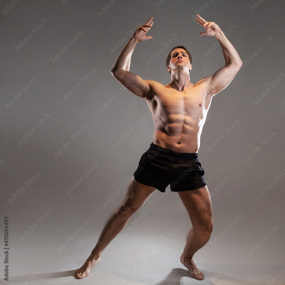A young muscular man in an expressive pose. Beautiful muscles. extraordinary athletic body. Portrait on a gray background