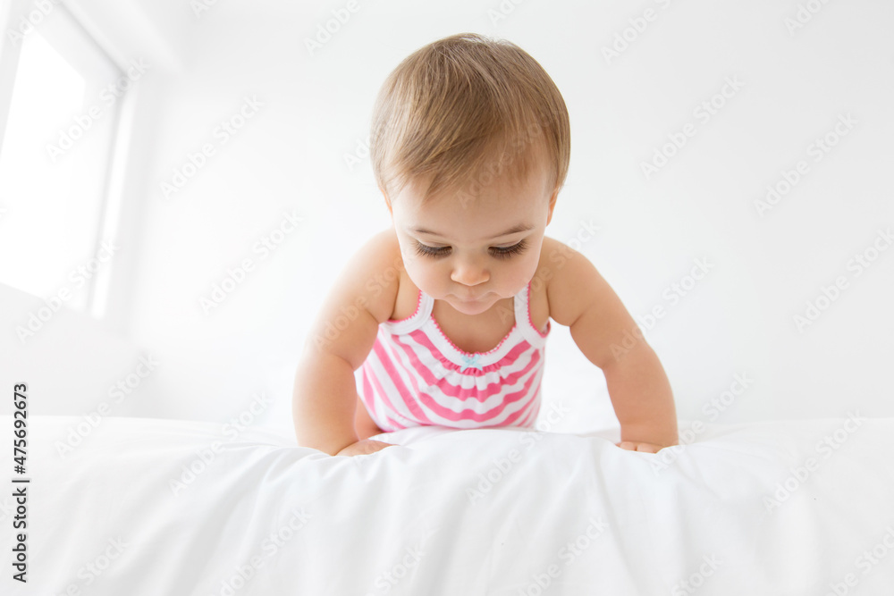 Cute baby girl crawling on white bed looking down Cute baby girl crawling on white bed looking down