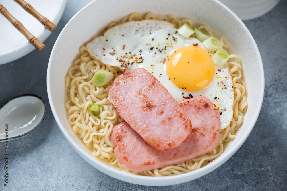 White bowl with Hong Kong breakfast made of ramen, fried egg and meat, middle close-up, elevated view White bowl with Hong Kong breakfast made of ramen, fried egg and meat, middle close-up, elevated view