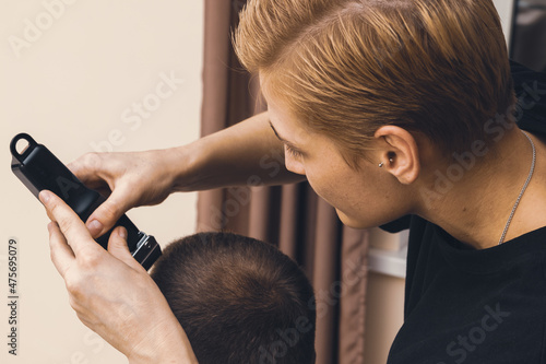 The woman hairdresser uses a hair clipper for cutting the man.