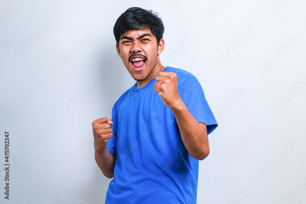 Asian man very happy and excited doing winner gesture with arms raised, smiling and screaming for success Asian man very happy and excited doing winner gesture with arms raised, smiling and screaming for success
