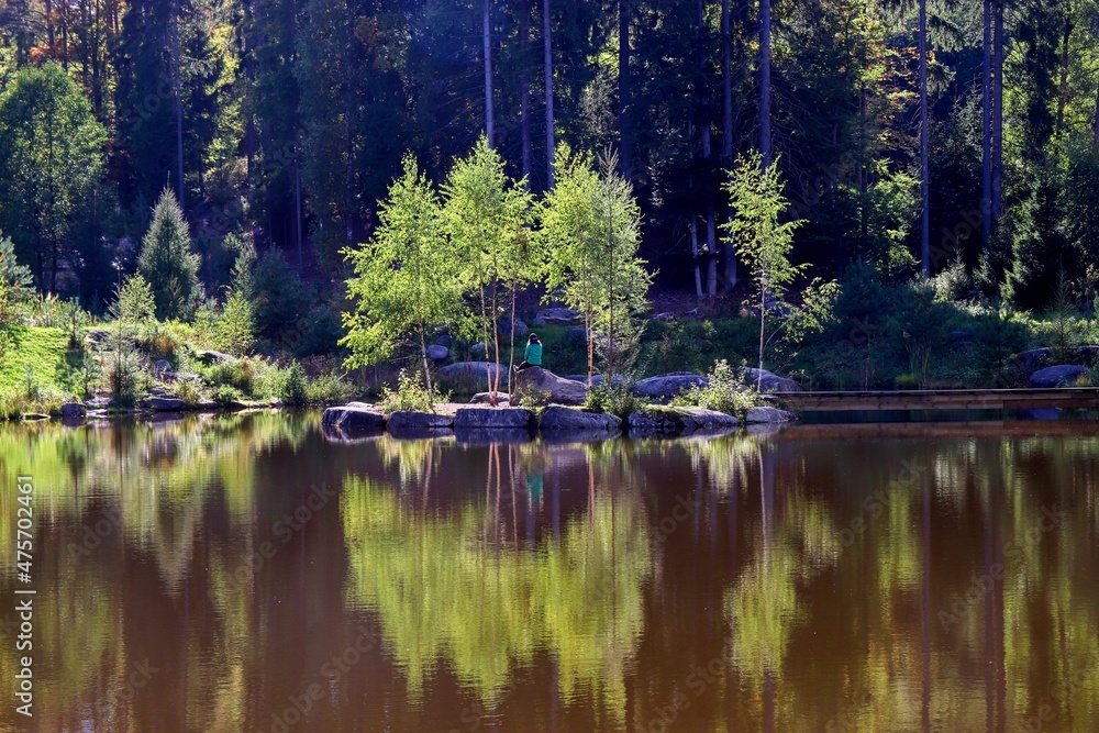 A girl sitting on the little island in the middle of a lake with beautiful water reflection near Cesky Rudolec, Czech republic