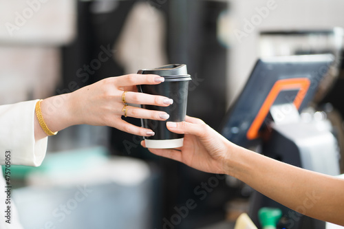 Caucasian waitress, a small company owner, a barista, and a bartender serving customer a coffee up at the bar counter in a cafe shop. Close Up hand holding a coffee cup