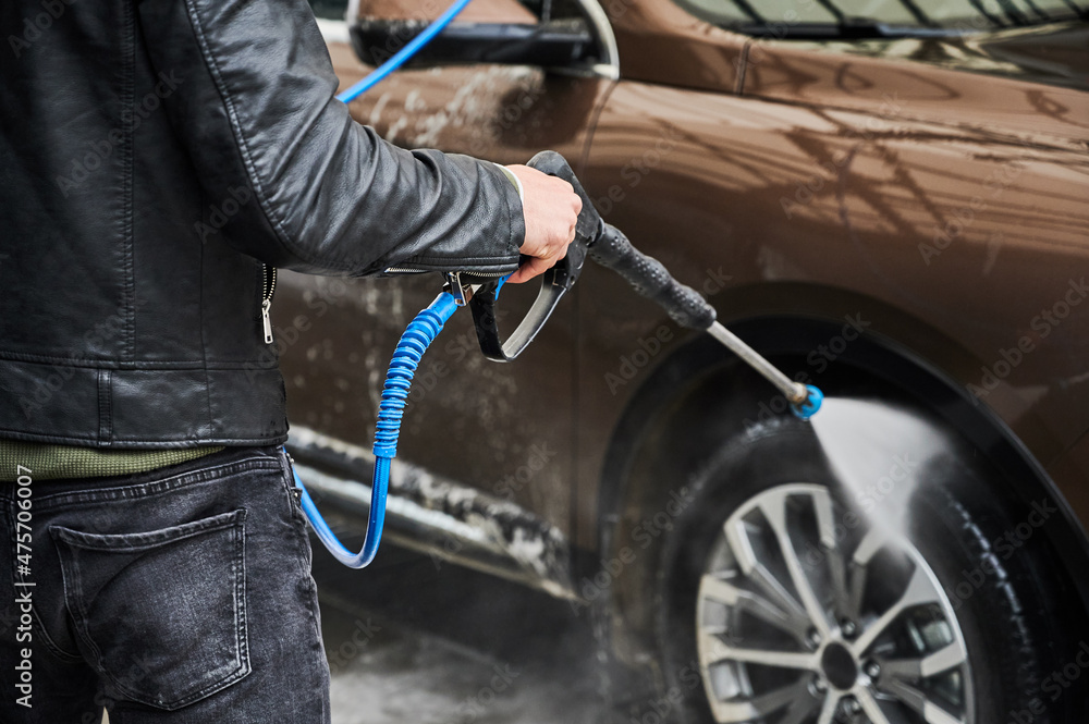 Obraz premium Cropped view of man washing car on carwash station outdoor. Driver cleaning automobile, using high pressure water.