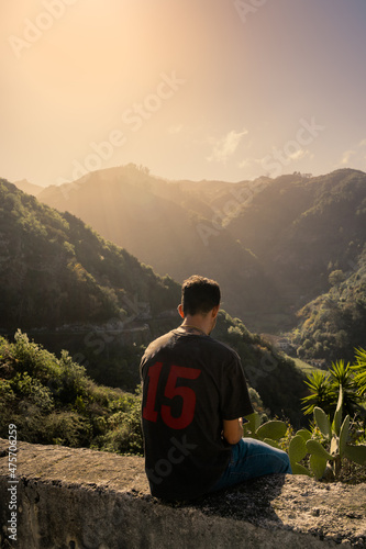 young man sits on a wall to watch the sunset in the mountains. vertical composition