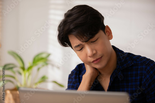 Working online at home on a laptop desk has given an Asian businessman a headache and fatigue.