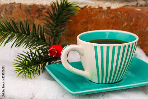 Green set cup with a saucer with black coffee near the Christmas tree artificial branch in the snow 