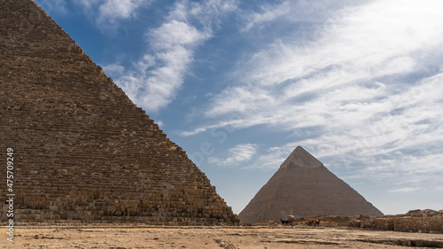 Two ancient Egyptian pyramids  Cheops and Chephren on a background of blue sky and clouds. The masonry walls are visible.  There are horse-drawn carts at the foot. Egypt