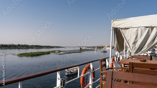 Wooden tables and chairs are installed on the upper deck of the cruise ship. From the deck you can see the Blue Nile River, green shores and the island.Boats on the water. Clear azure sky. Egypt photo