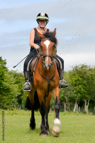 Middle aged woman riding her horse in the summer sunshine 