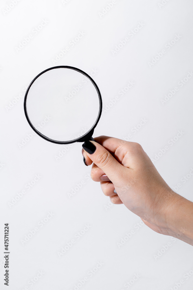 Female hand holding a magnifying glass with black frame on a white background Female hand holding a magnifying glass with black frame on a white background
