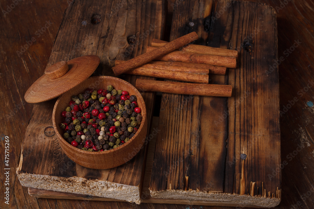 Pot of aromatic pepper set, allspice peas, cinnamon sticks on wooden kitchen board on country table. Flavourings, seasonings Pot of aromatic pepper set, allspice peas, cinnamon sticks on wooden kitchen board on country table. Flavourings, seasonings