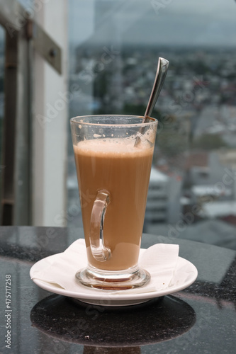 A glass of coffee latte on a table against a blurred background.