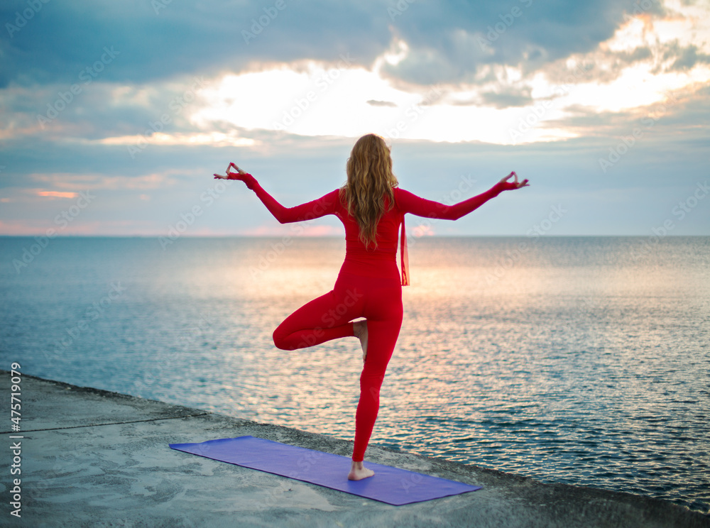 Obraz premium one-legged yoga asana, on the embankment near the sea at dawn with clouds in the sky