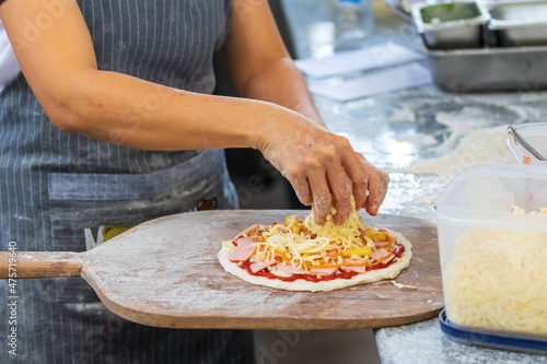 people and cooking concept - cook hand adding grated cheese to pizza at pizzeria