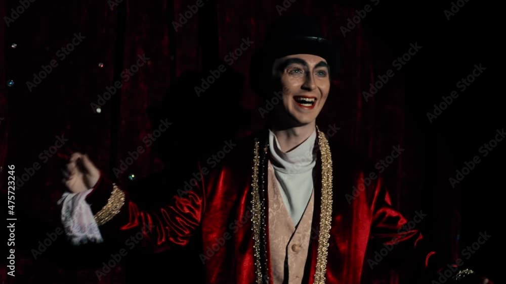 Portrait of an admiring showman A guy, a magician with make-up in a red dress coat, looks surprised into the hall. Portrait of an admiring showman A guy, a magician with make-up in a red dress coat, looks surprised into the hall.