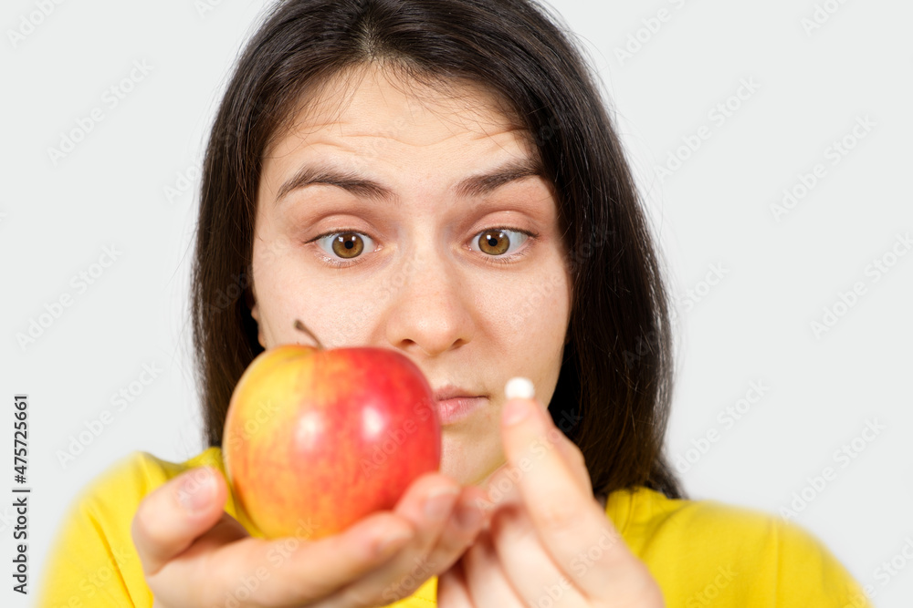 A woman in yellow holds an apple and a pill in her hands. Vitamins in natural form and in synthetic, dietary supplements A woman in yellow holds an apple and a pill in her hands. Vitamins in natural form and in synthetic, dietary supplements